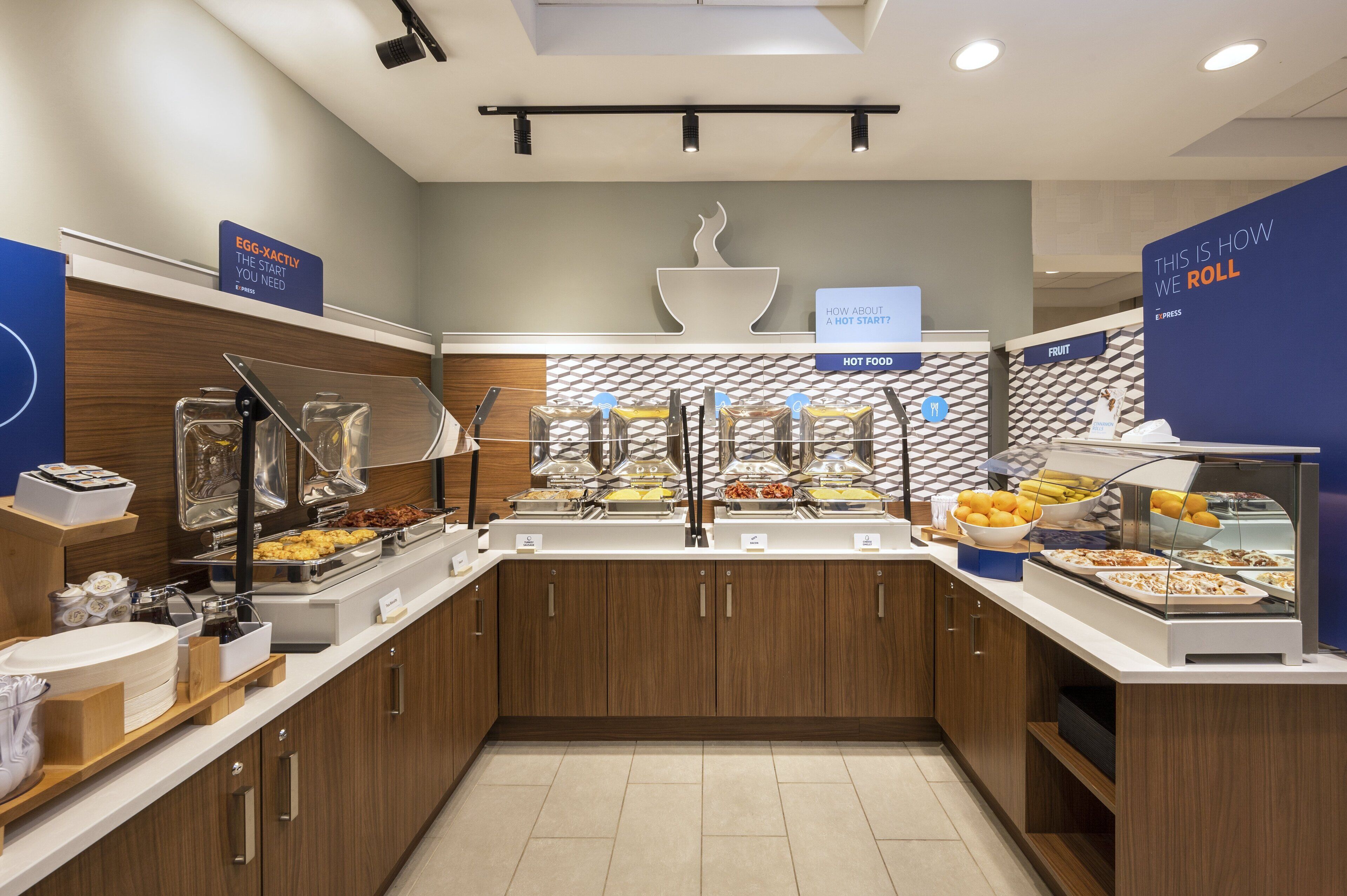 A buffet setup with various food stations, including hot food and fruit sections, and a sign indicating the start of the buffet.