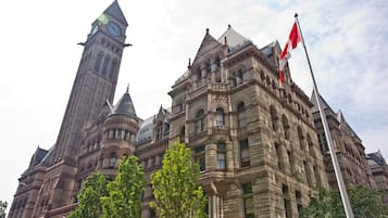 A historic building with intricate stonework, a prominent clock tower, and a flagpole.