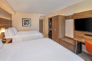 A hotel room with two beds, a desk with a flat-screen TV, a wardrobe, and a coffee machine.