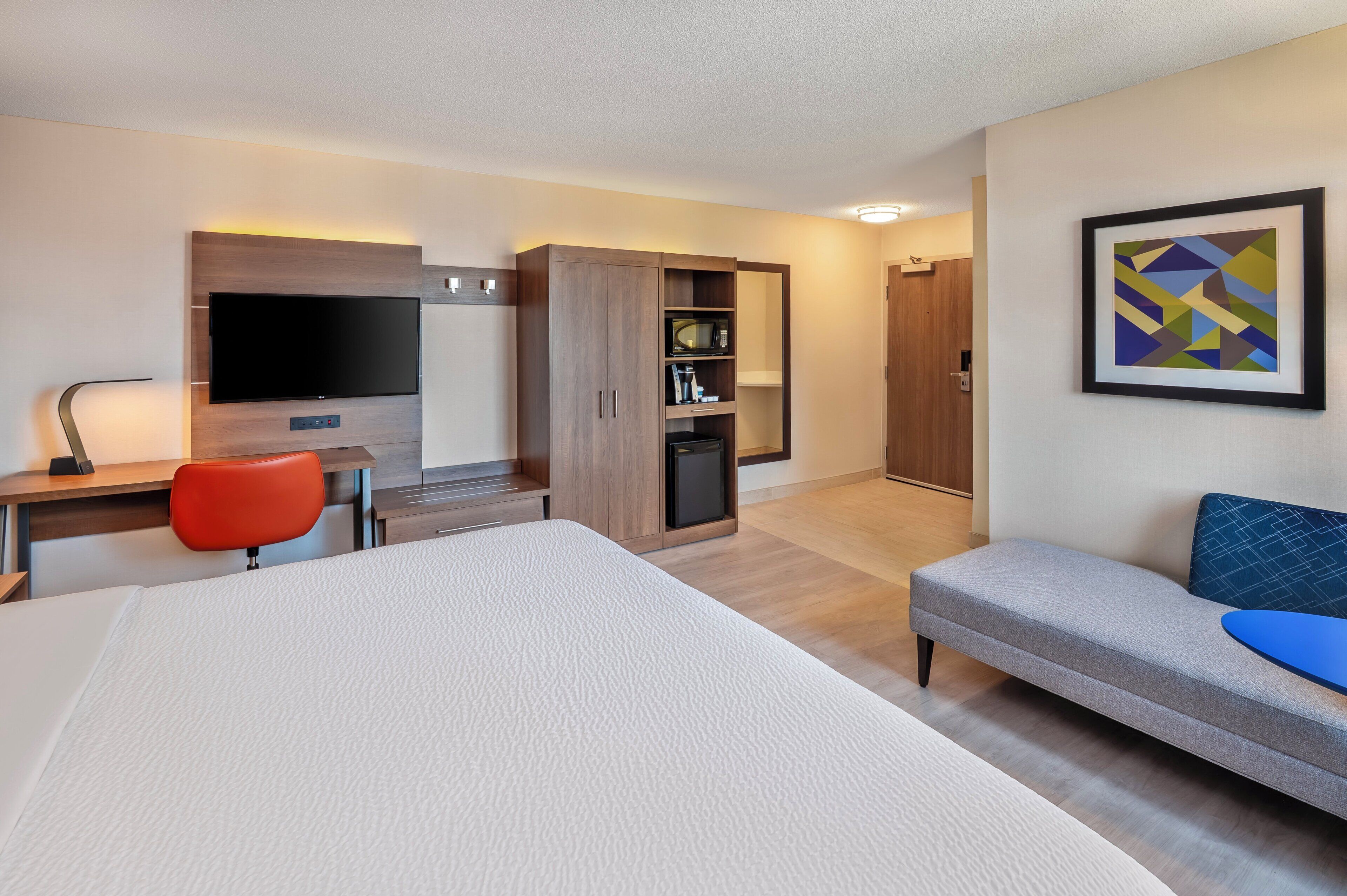 Une chambre d’hôtel comprenant un lit, un bureau avec une télévision, une armoire et un canapé.