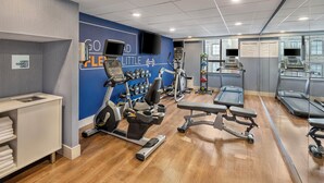 Un gimnasio con equipo cardiovascular, máquinas de pesas y un espejo grande.