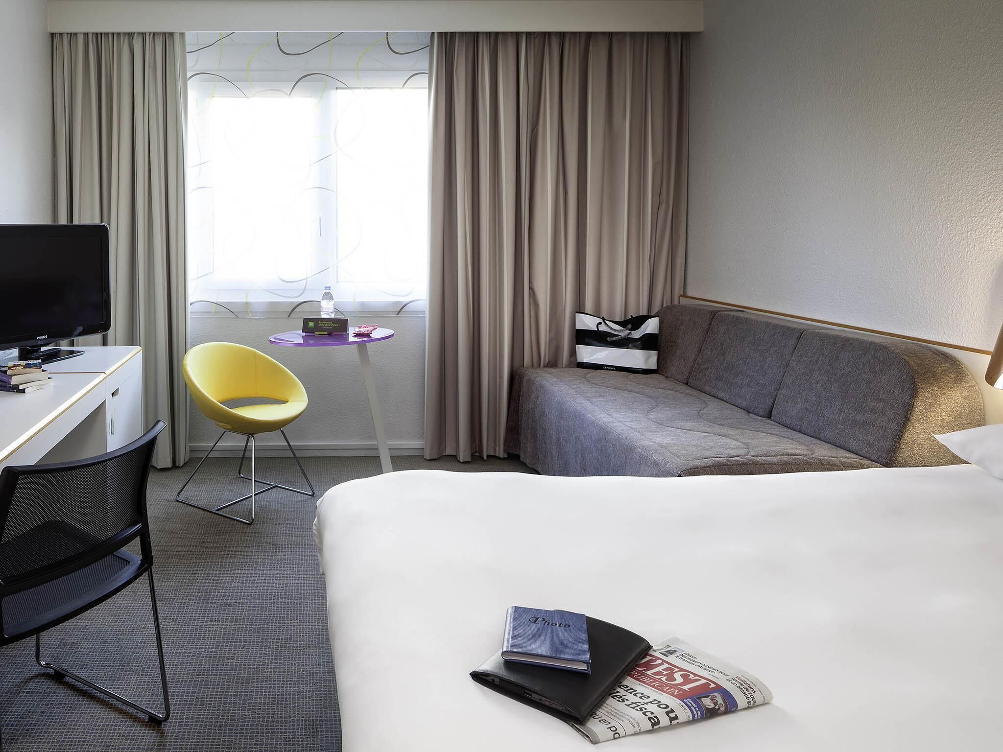 Een hotelkamer met een bed, bureau, stoel, bank en raam met gordijnen.