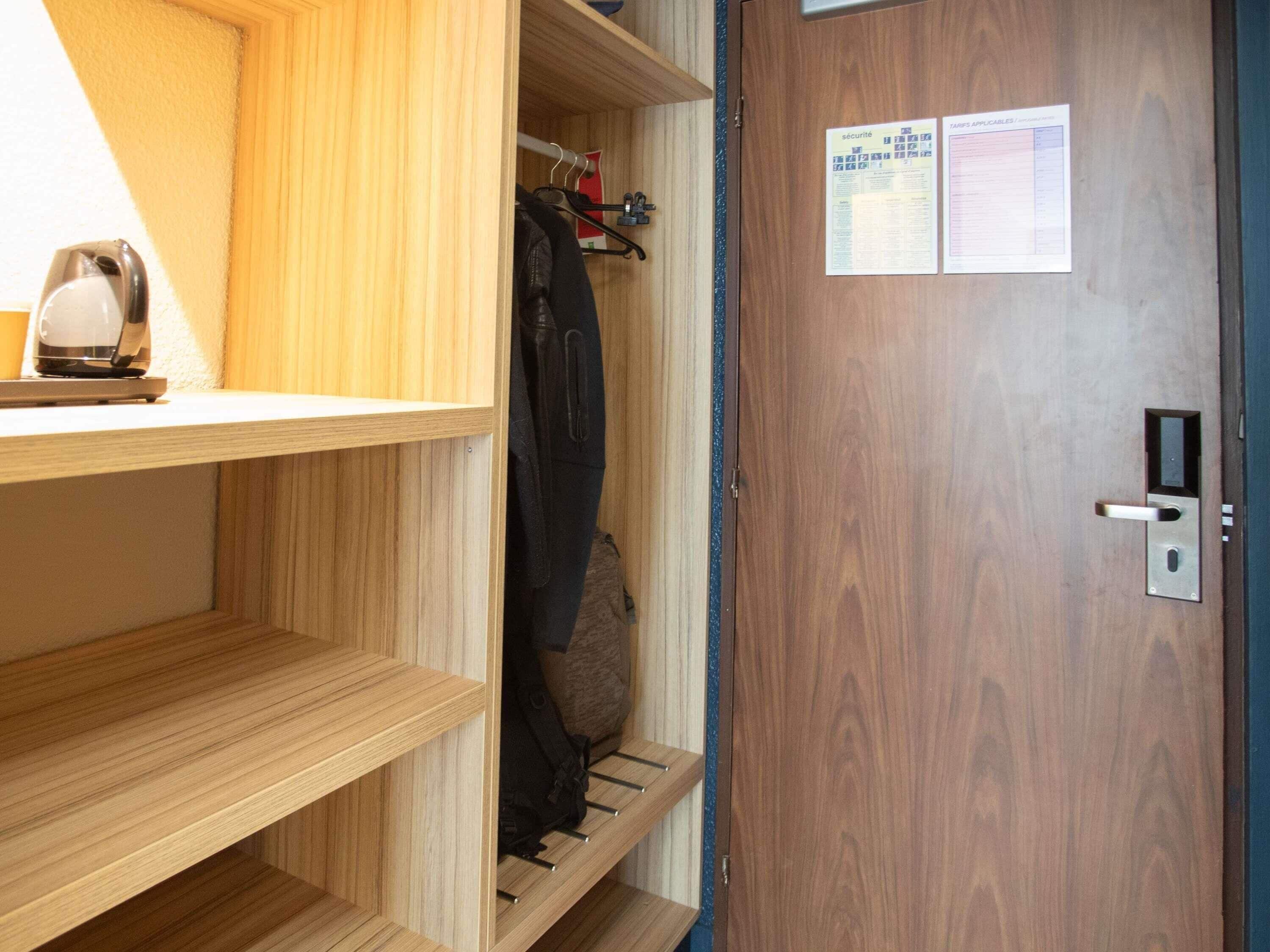 A wooden closet with shelves and hanging space, a door with a security card reader, and a kettle on the counter.