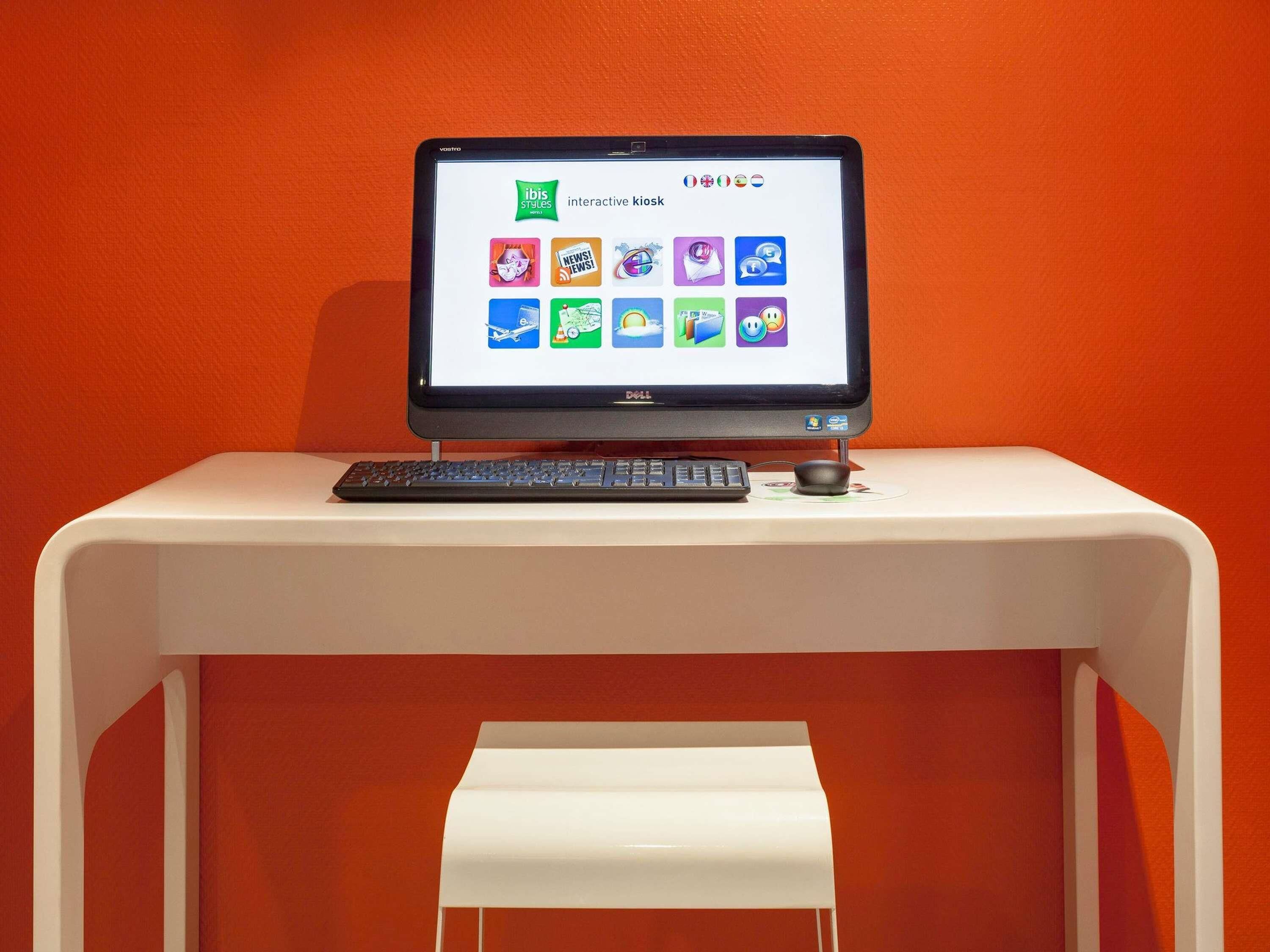 Un monitor Dell sobre un escritorio blanco frente a una pared naranja.