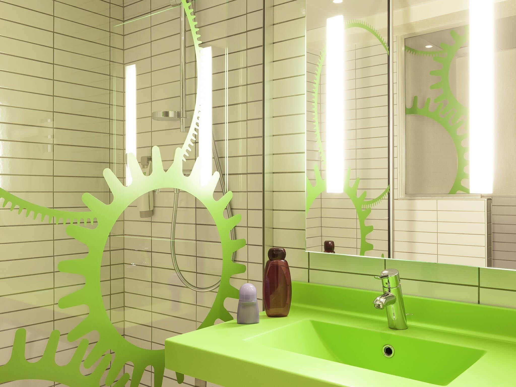 A bathroom with a green sink, a mirror, and a shower with a green gear-shaped showerhead.