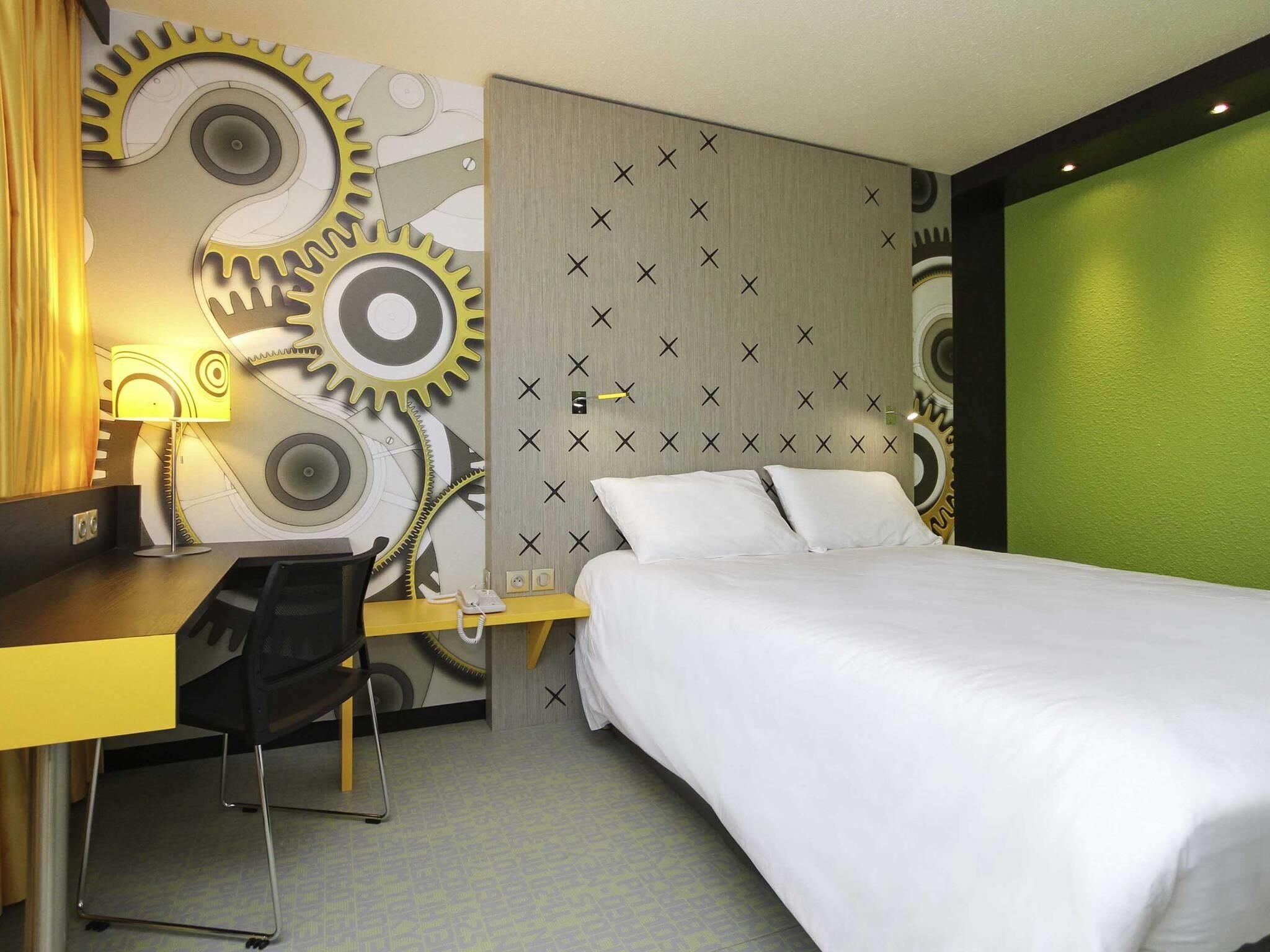 A hotel room with a bed, desk, and chair. The room features a unique wall design with gears and crosses.