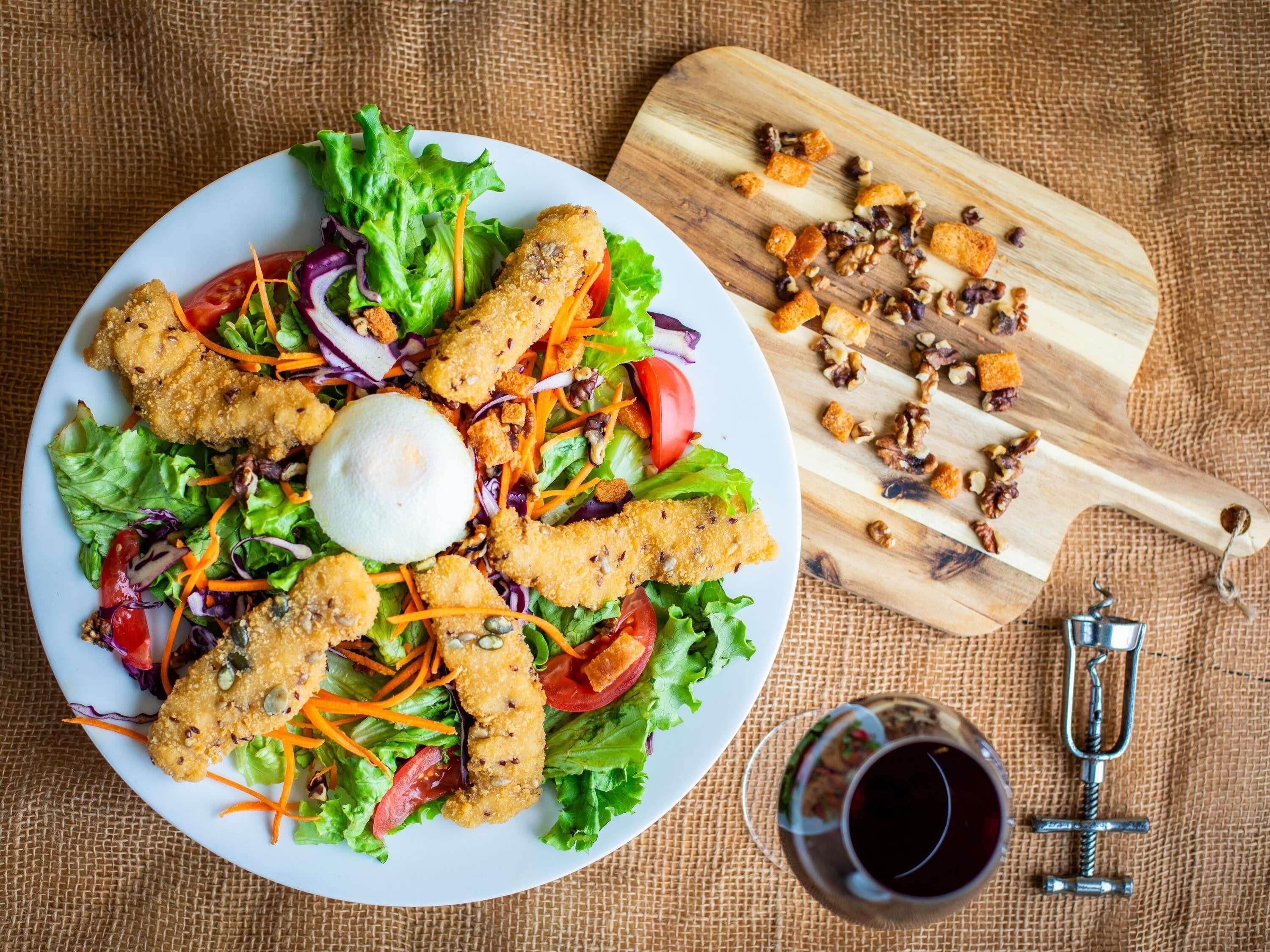 Ensalada con crutones y nueces sobre un plato blanco, junto a una tabla de cortar de madera y un abrelatas metálico.