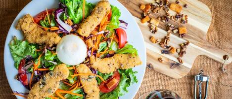 Ensalada con crutones y nueces sobre un plato blanco, junto a una tabla de cortar de madera y un abrelatas metálico.