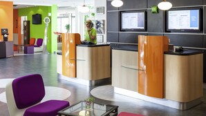 A modern hotel reception area with a reception desk, seating area, and digital information displays. - ibis Styles Besançon (Besancon)
