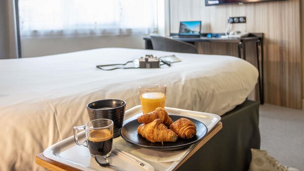 A hotel room with a bed, a tray with croissants, a glass of juice, and a cup of coffee. - ibis Styles Besançon (Besancon)