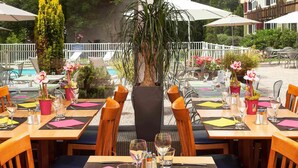 An outdoor dining area with tables set for two, surrounded by potted plants and umbrellas. - ibis Styles Besançon (Besancon)