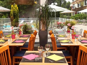 An outdoor dining area with tables set for two, surrounded by potted plants and umbrellas. - ibis Styles Besançon (Besancon)