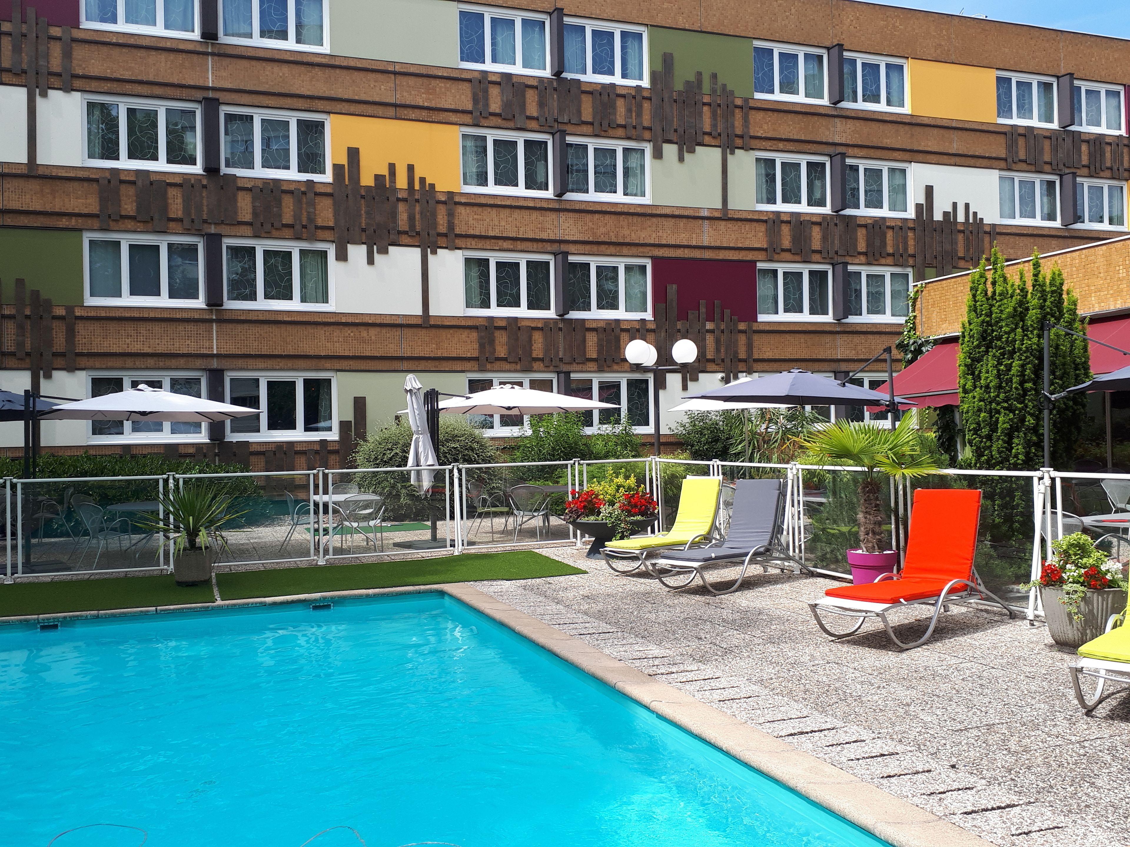 Un hotel con piscina, mobiliario exterior y un edificio de varios pisos con balcones.