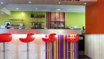 A bar area with a counter, stools, and shelves with bottles and glasses.
