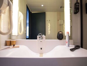Bathroom features a large mirror, a central sink with a faucet, and a hairdryer.