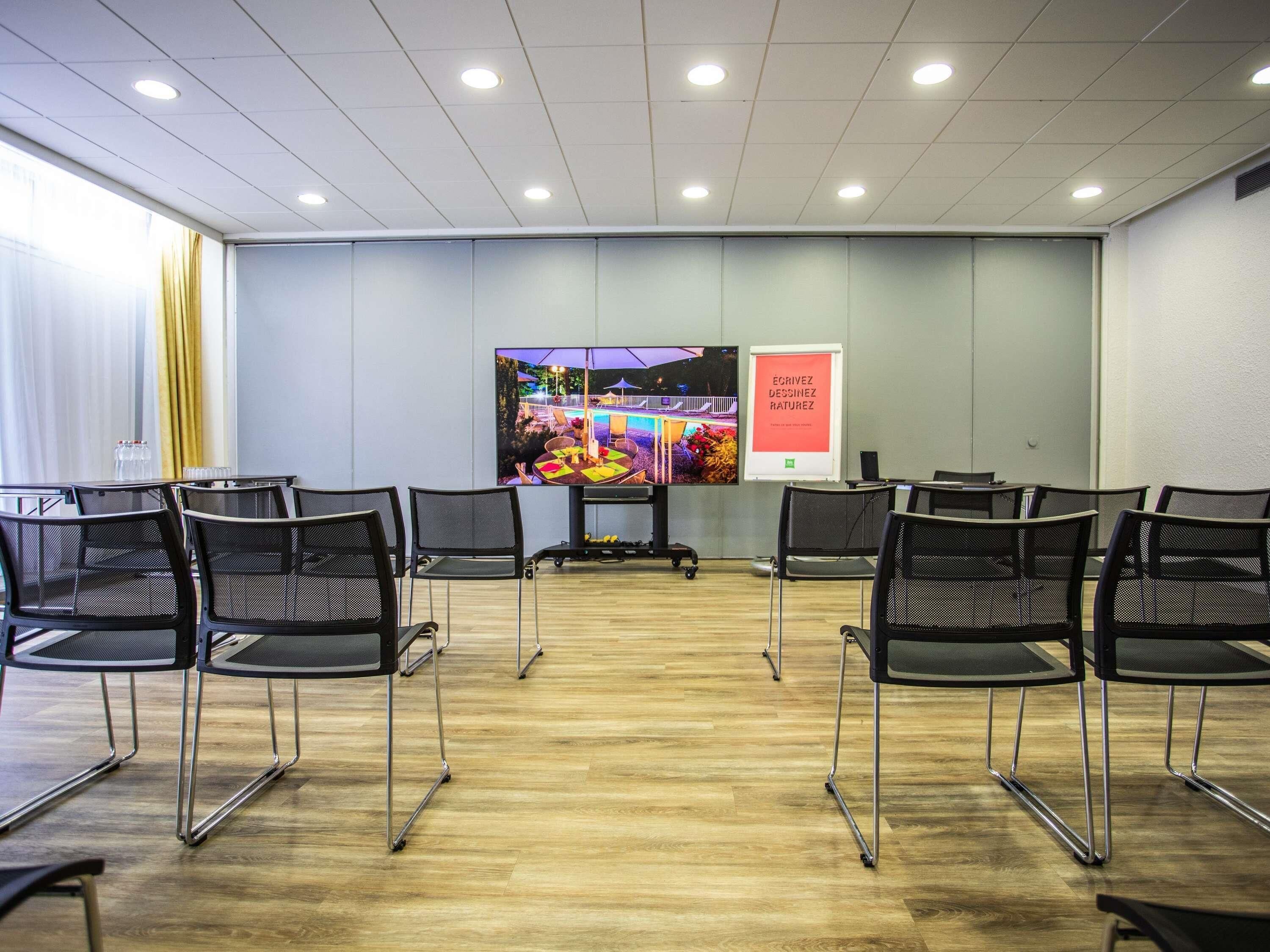 A conference room with a large screen, chairs, and a poster on the wall.