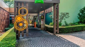 The entrance to ibis Styles Hotel in Besançon, featuring a covered walkway, a green banner, and a distinctive sun-like sculpture. - ibis Styles Besançon (Besancon)