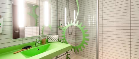 Un baño con un lavamanos verde, un espejo y una ducha con cabezal en forma de engranaje verde.