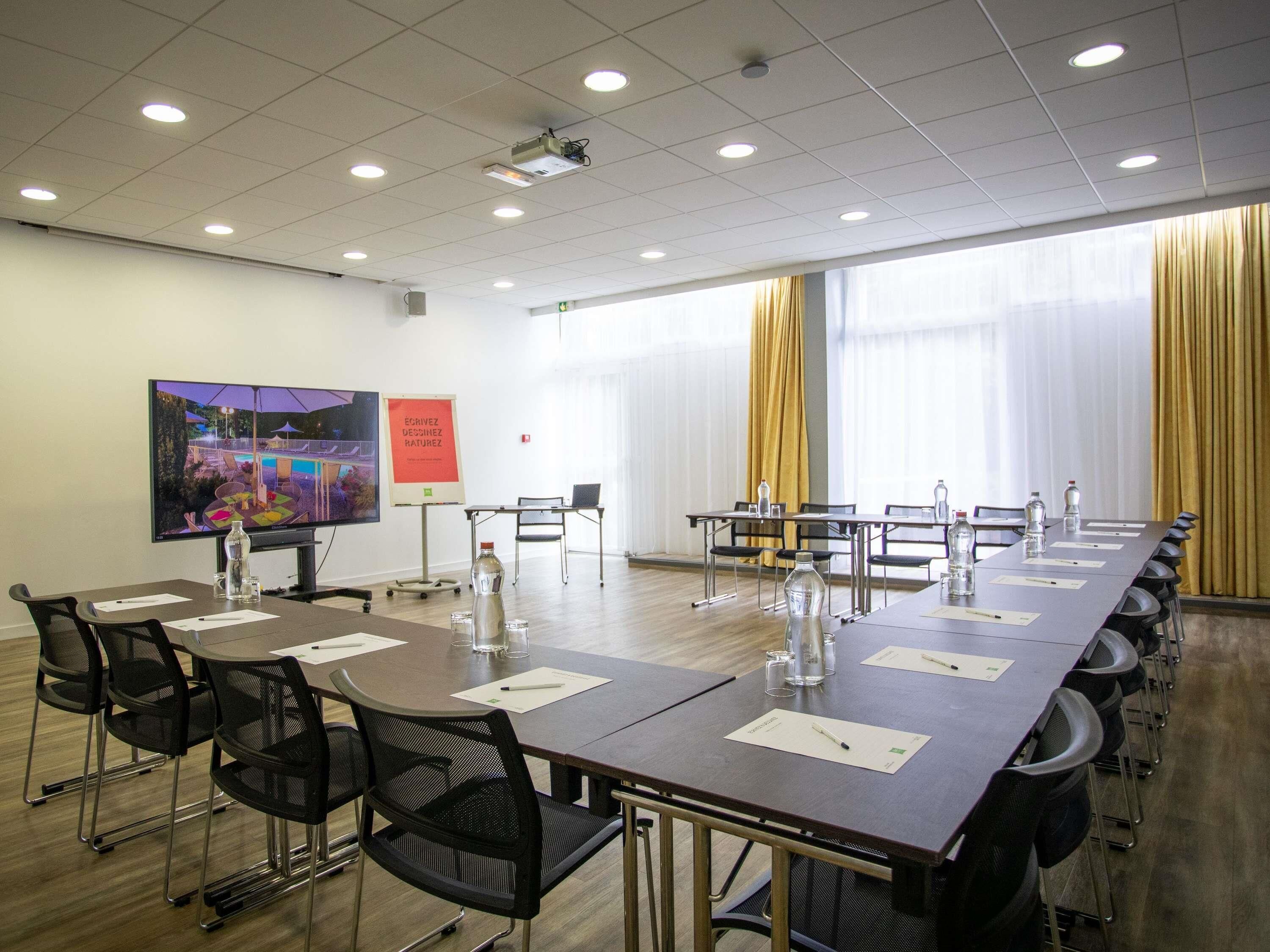 Un salón de conferencias con una larga mesa, sillas, un proyector, una pantalla y una pizarra.