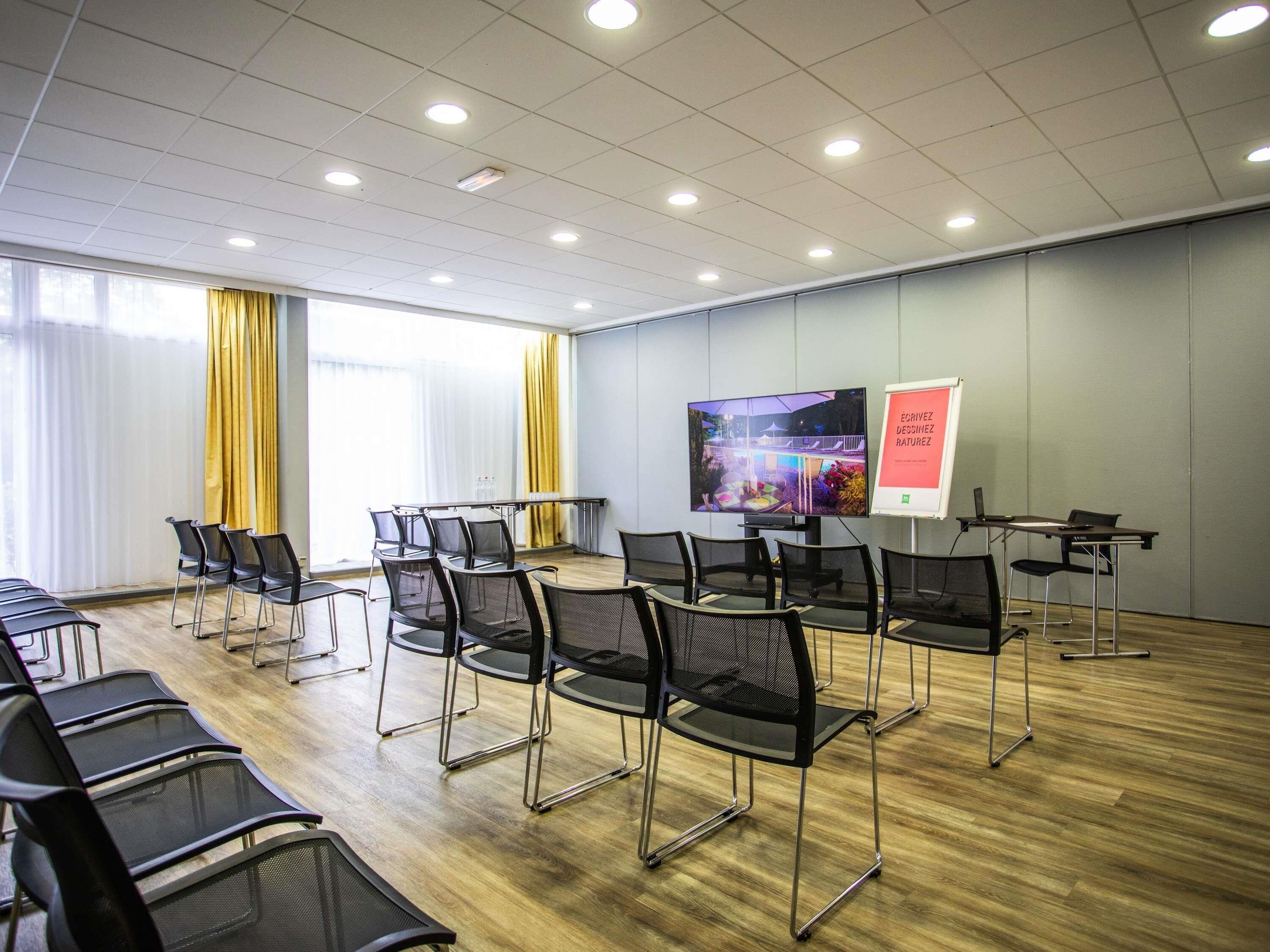 A conference room with a large screen, chairs, tables, and a whiteboard.