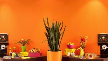 Un comptoir d’accueil avec une machine à café, un saladier de fruits, une plante en pot et un vase rempli de fleurs.