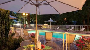 An outdoor pool area with lounge chairs, a dining table set for two, and umbrellas providing shade. - ibis Styles Besançon (Besancon)