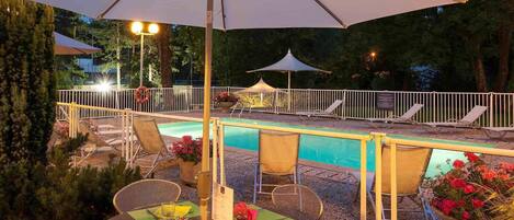 Un área de piscina al aire libre con sillones de descanso, una mesa de comedor para dos personas y sombrillas que dan sombra.
