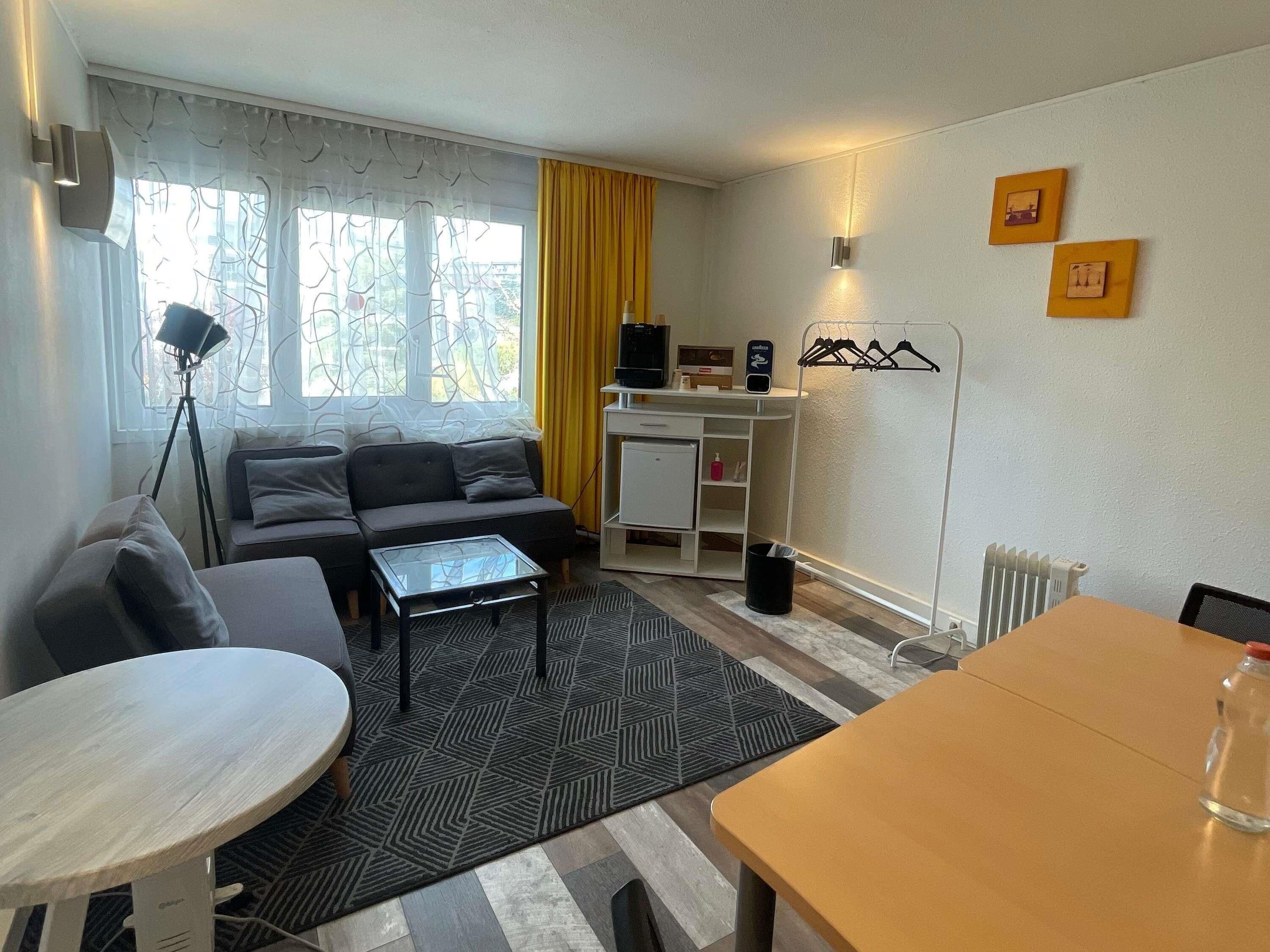 A compact living space with a sofa, a small table, a radiator, and a desk with a computer.