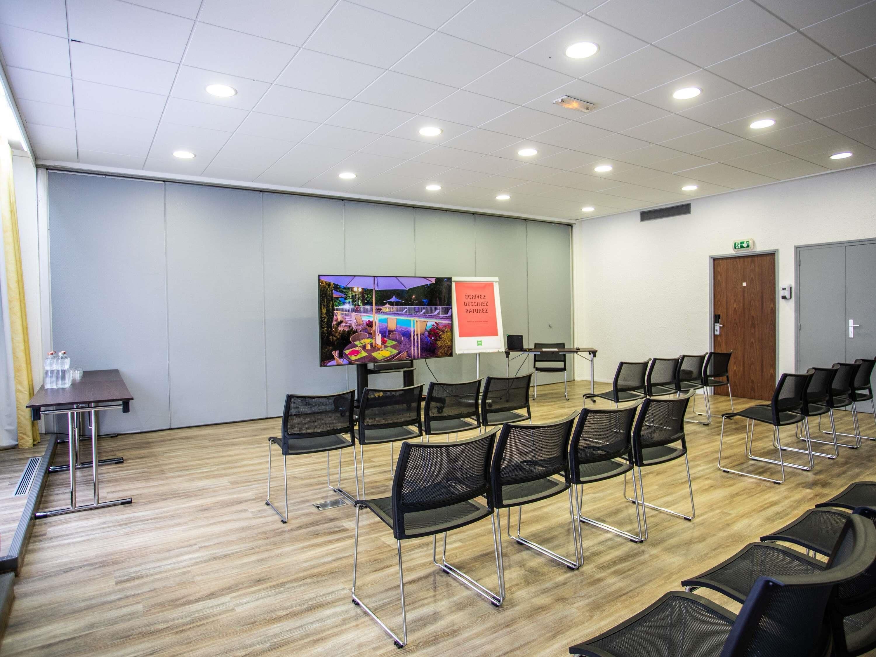 Une salle de conférence équipée d’un grand écran, de chaises, d’une table et d’un panneau indicateur.