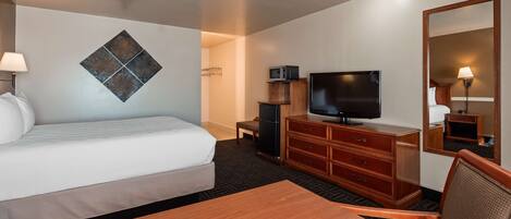 A hotel room with a bed, a TV, a dresser, a desk, and a mirror.