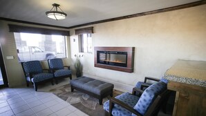 A living room with a fireplace, two blue patterned armchairs, a grey ottoman, and a wooden coffee table. - Best Western Paradise Inn (Beaver)