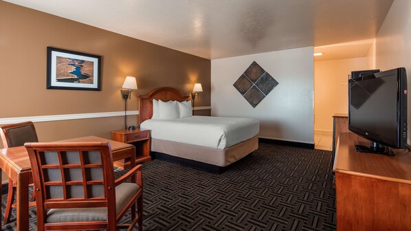 A hotel room with a bed, a desk with a chair, a television, and a framed picture on the wall.