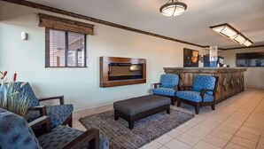 A living room with a TV, two blue patterned chairs, a dark ottoman, and a wooden bar area. - Best Western Paradise Inn (Beaver)