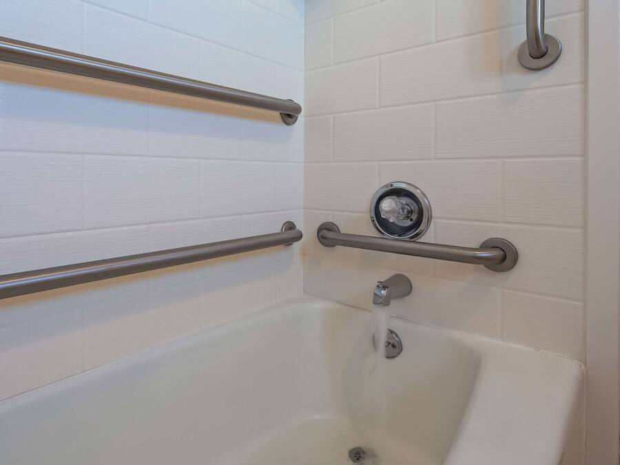 A bathtub with two metal grab bars, a faucet, and a drain.