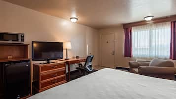 Ett hotellrum med en säng, ett skrivbord med en dator, en TV, en mikrovågsugn och en minibar.