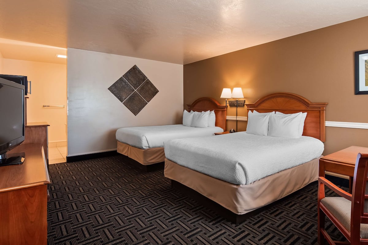 A hotel room with two beds, a TV, a desk, and a chair.