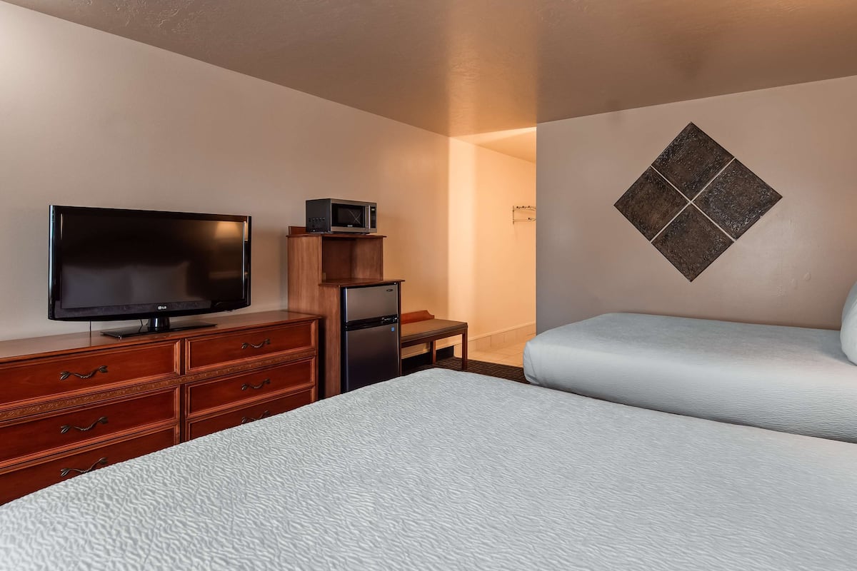 A hotel room with two beds, a television, a refrigerator, a microwave, and a wooden dresser.
