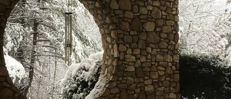 Un arco de piedra con abertura circular, a través del cual se aprecia un paisaje nevado y un árbol.