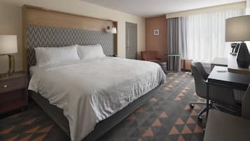 A hotel room with a large bed, a desk, a chair, a lamp, and a window with curtains.