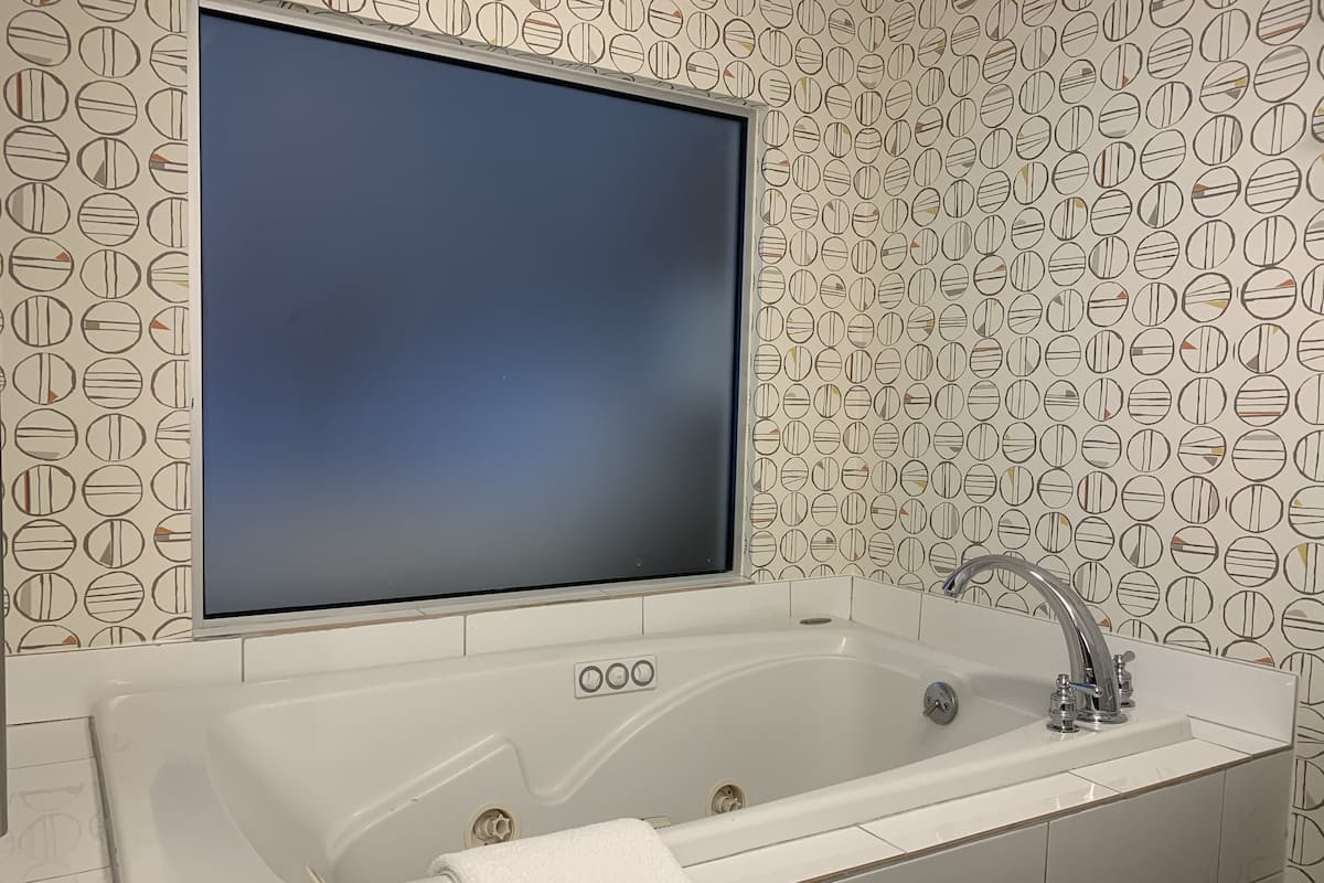 A bathroom with a large bathtub, a mirror, and a patterned wall.