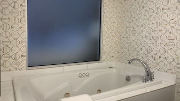 Een badkamer met een groot bad, een spiegel en een behang met patroon.