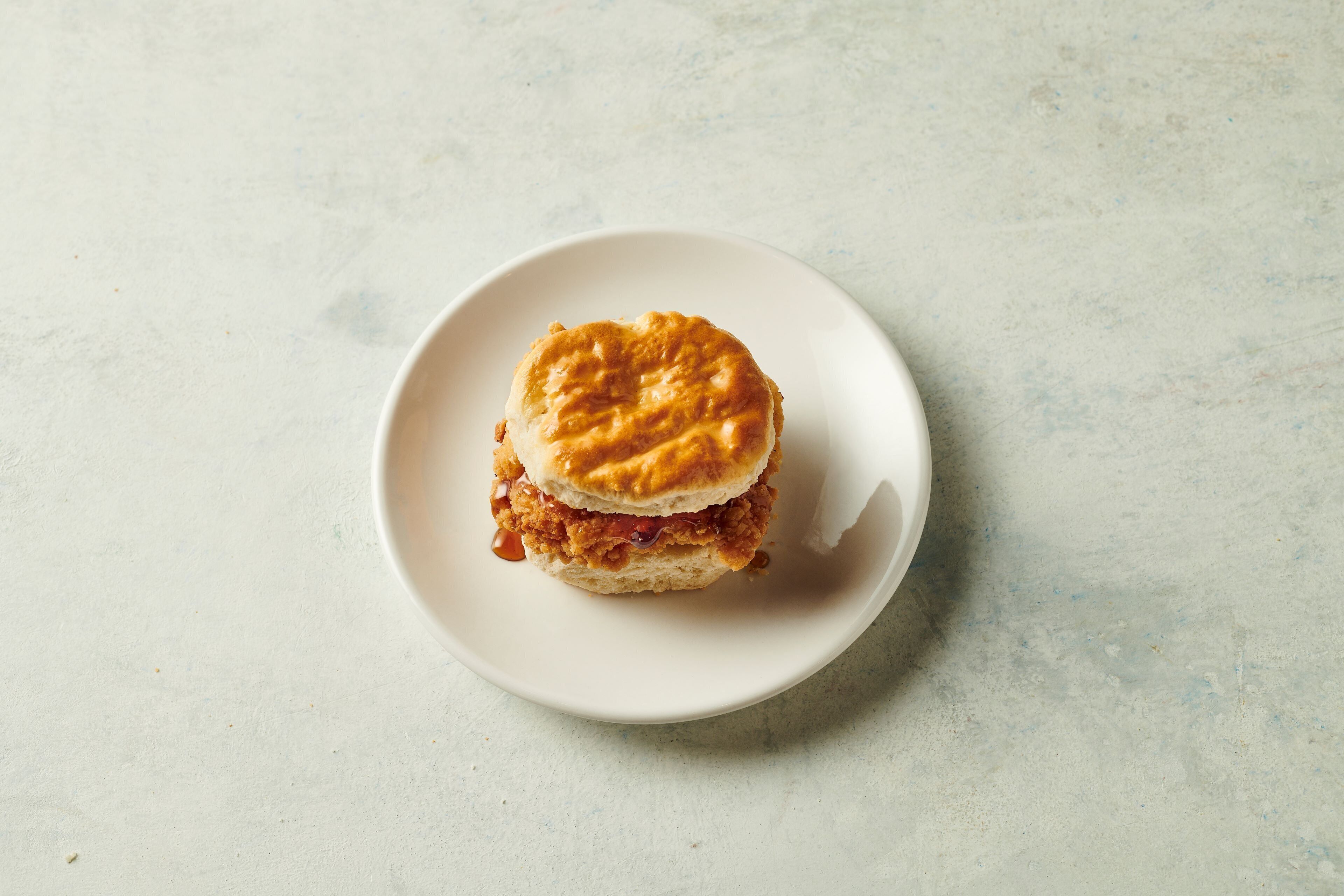Un sándwich de pollo solo sobre un plato blanco.