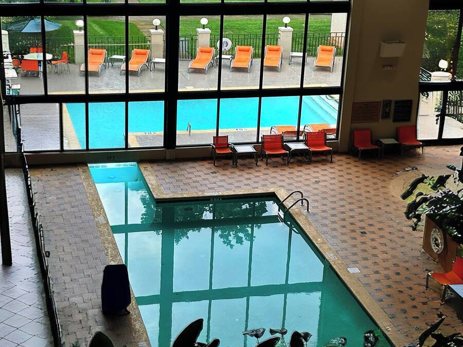 Ein Hallenbad mit mehreren Bahnen, Liegestühlen und Blick auf den Außenbereich durch große Fenster.