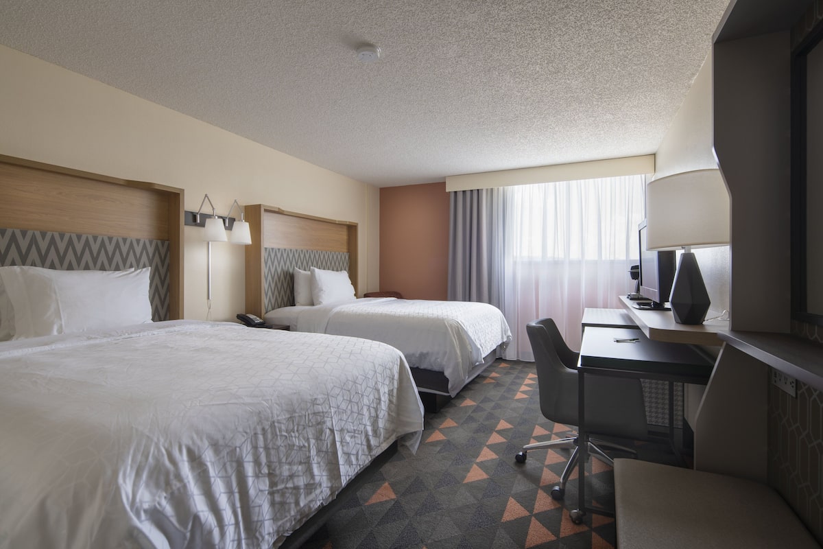 A hotel room with two beds, a desk, and a chair.