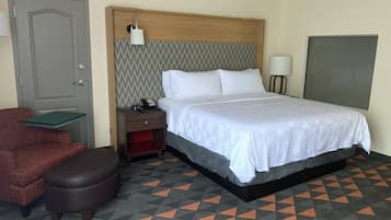 Una habitación de hotel con cama, mesita de noche, teléfono, silla y puerta.