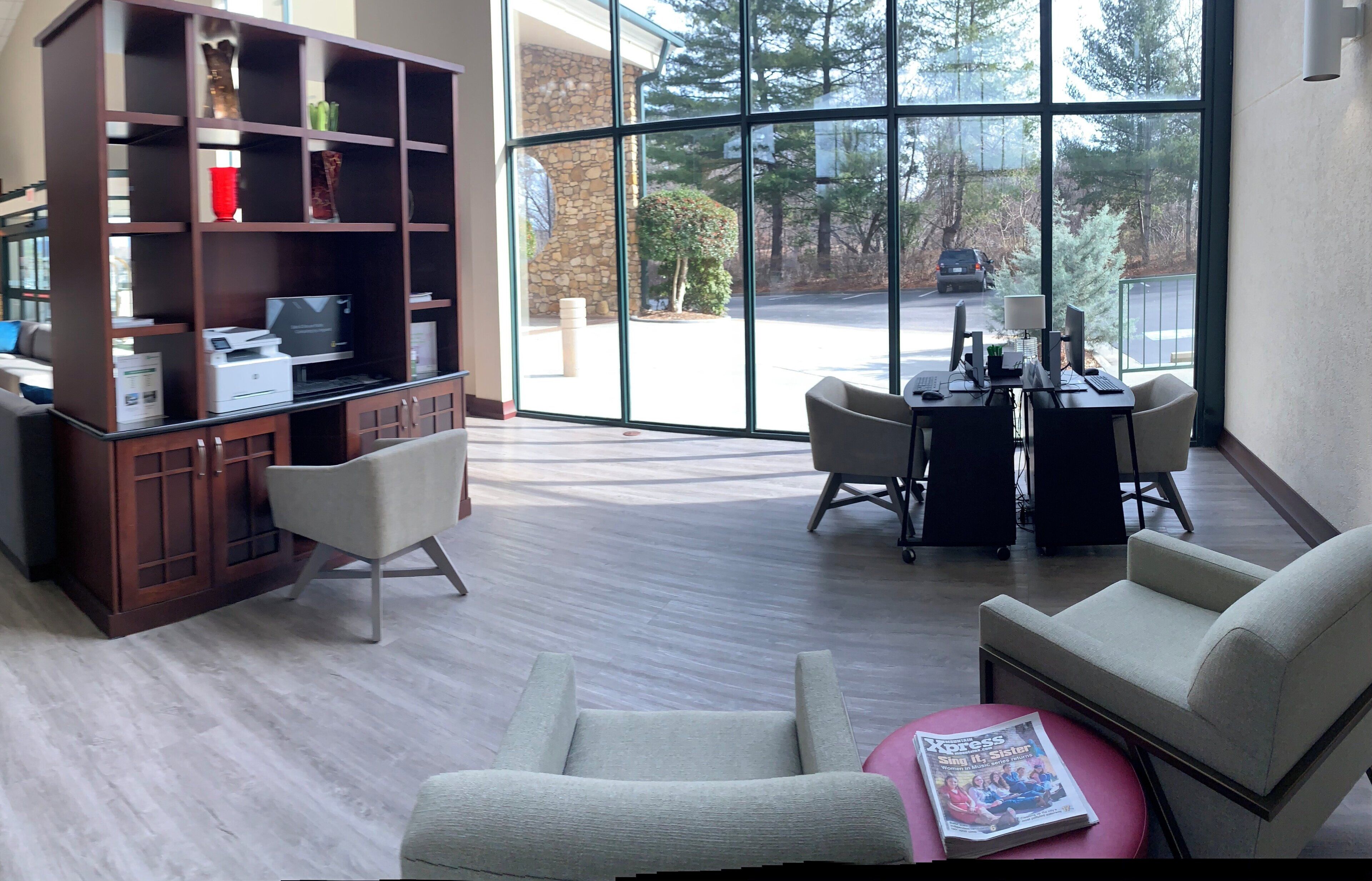 A spacious room with a large window, a wooden bookshelf, a desk with computers, and two chairs.