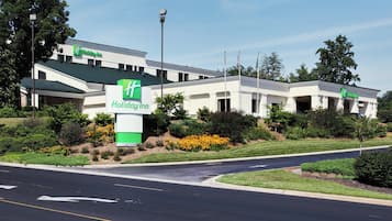 A Holiday Inn hotel with a green and white sign, surrounded by well-maintained landscaping and a clear sky.