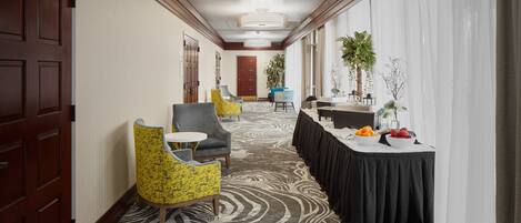 Un couloir d’hôtel avec un tapis à motifs, un comptoir d’accueil et des espaces aménagés avec des sièges.
