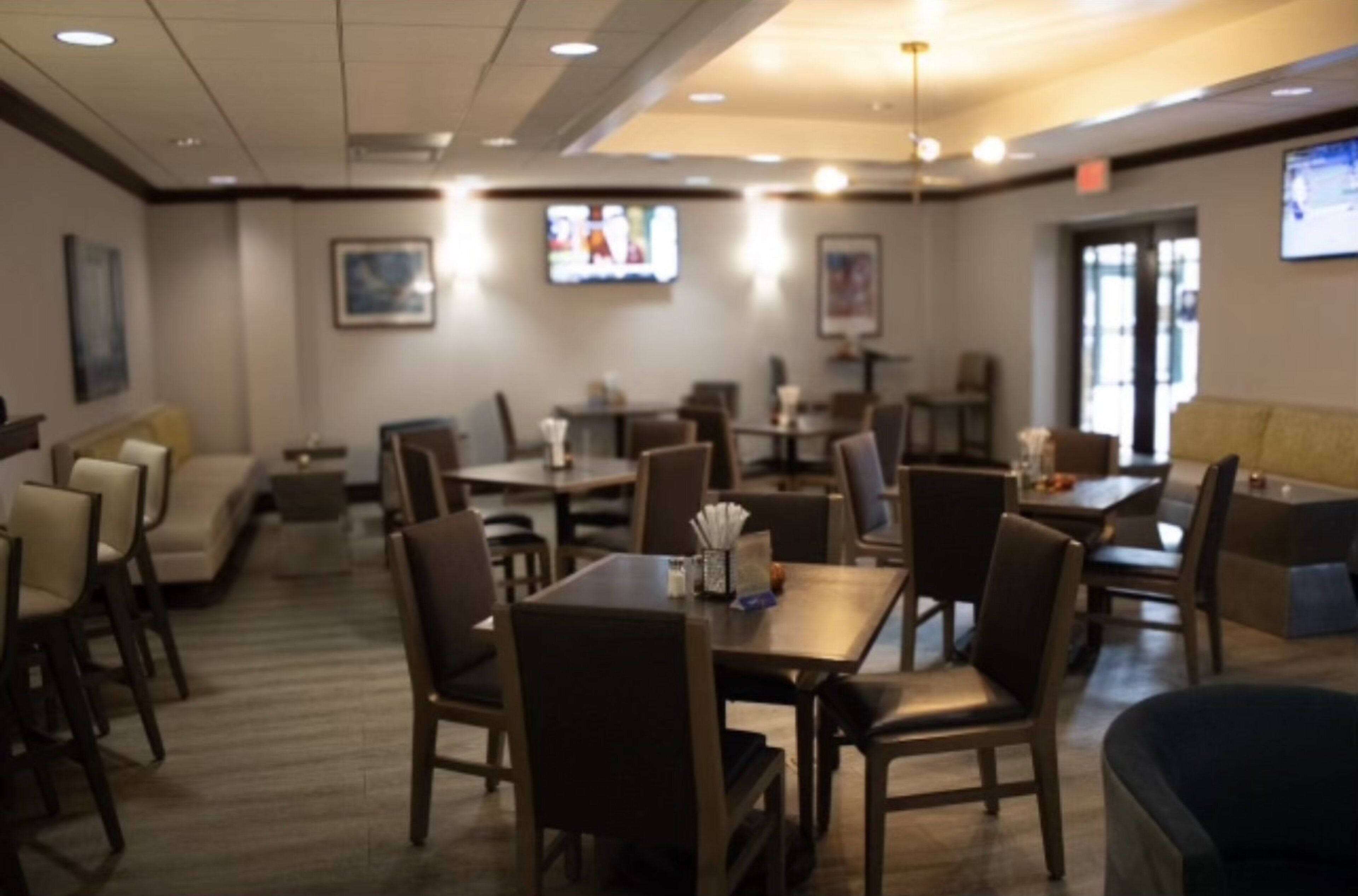 A restaurant with tables and chairs, a television screen, and a sofa.