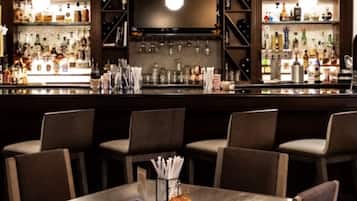 A bar area with multiple seating arrangements and a variety of bottles and glasses on the shelves.